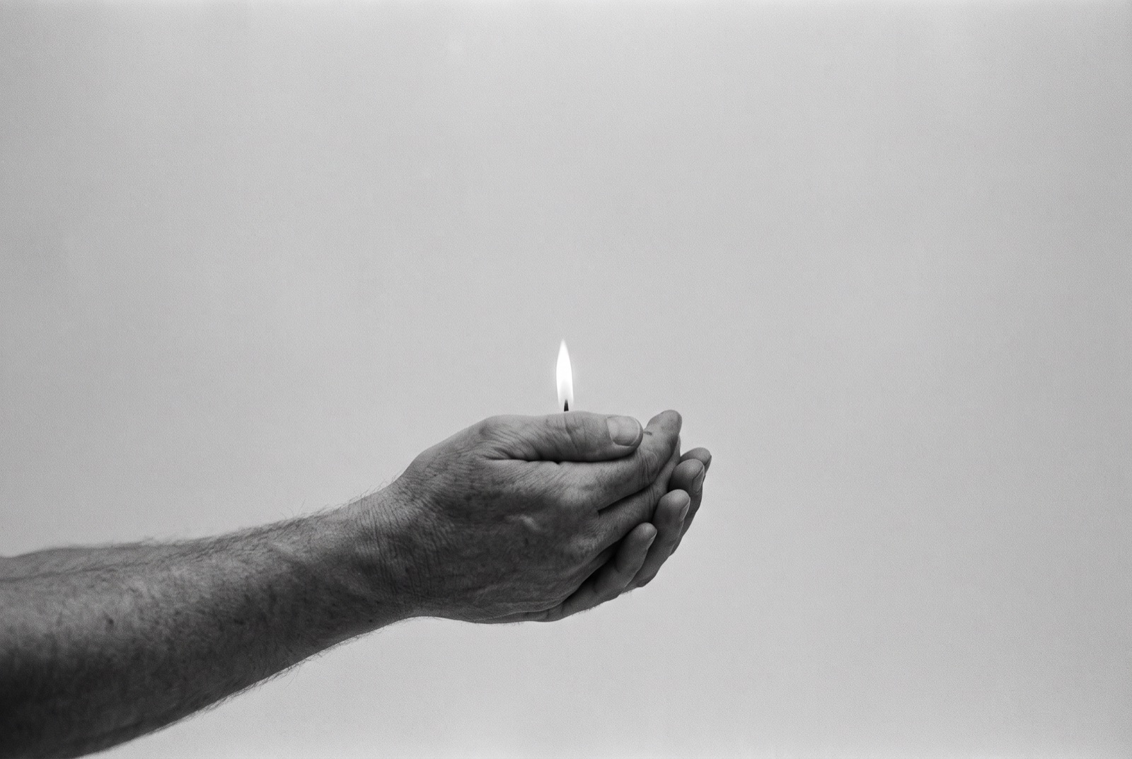 A pair of cupped hands holding a single small flame